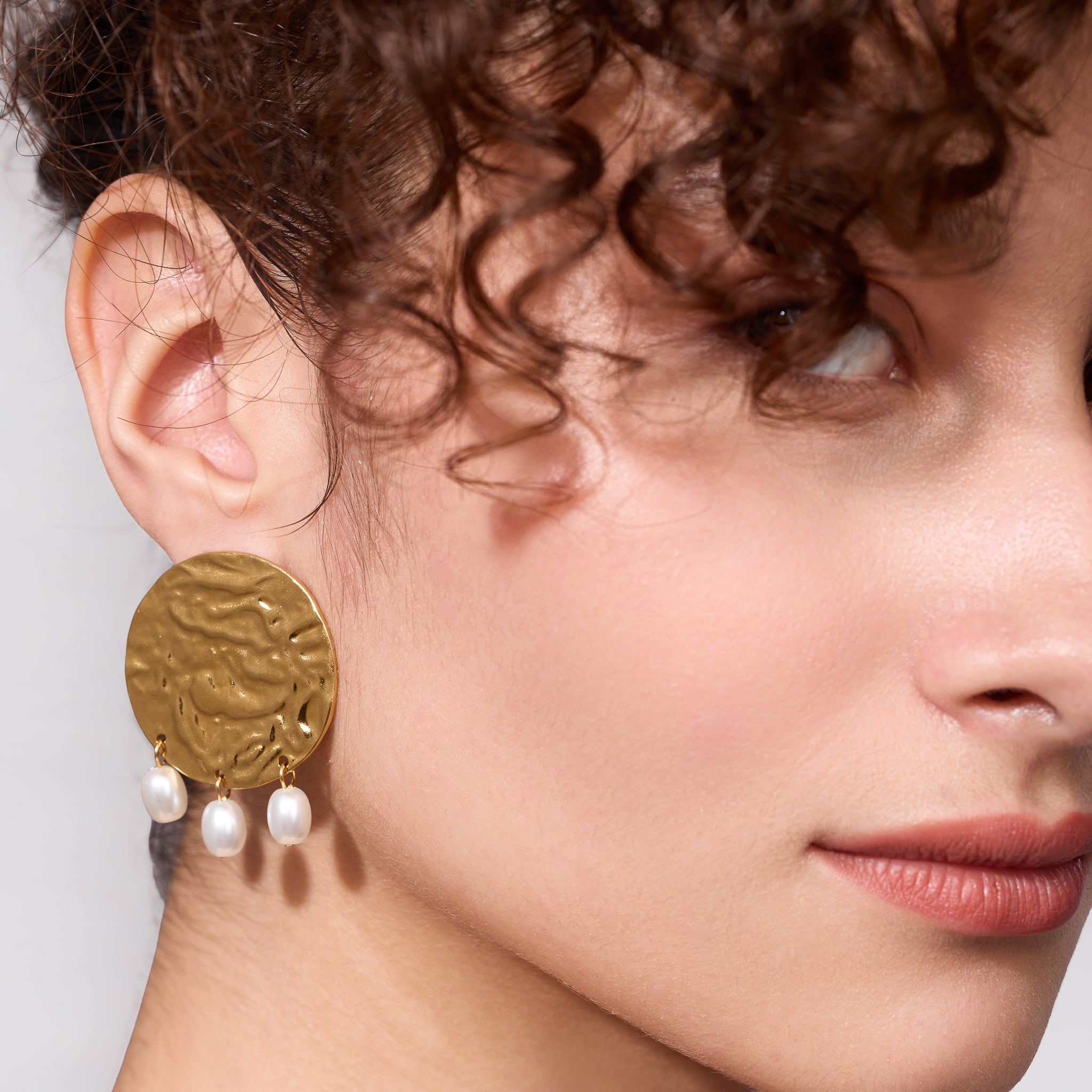 Close-up of a woman wearing gold earrings with pearl drops on a neutral background