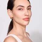 Woman wearing a gold earring against a plain background