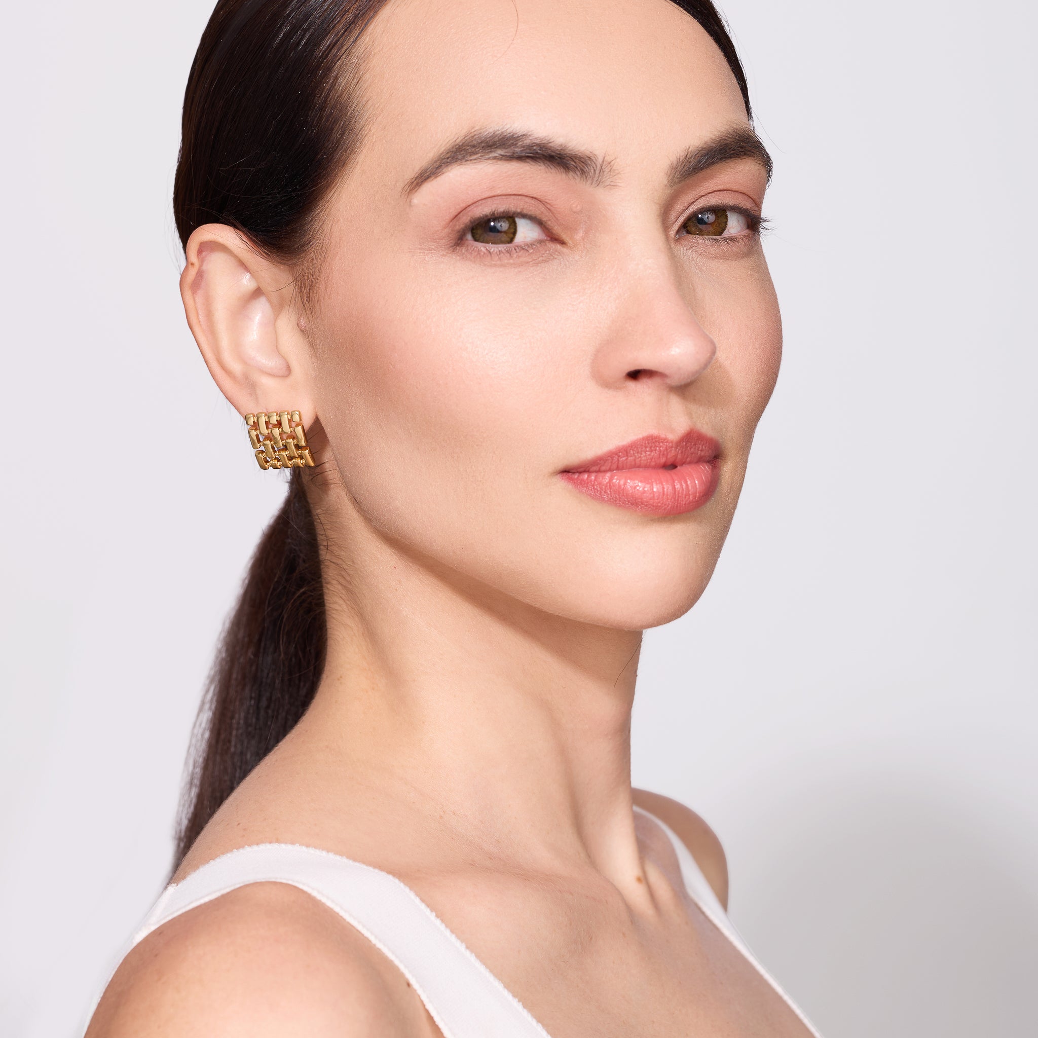 Woman wearing a gold earring against a plain background