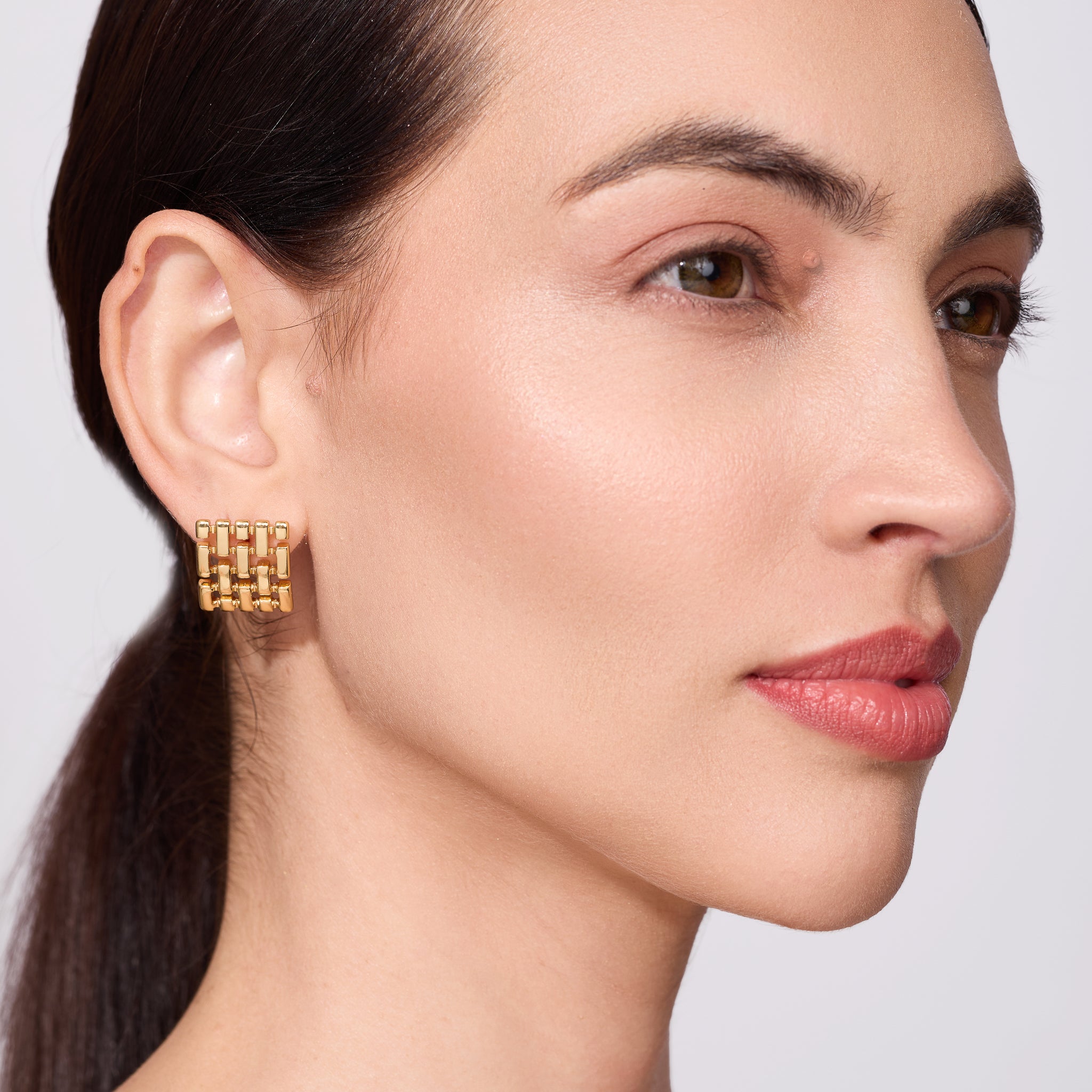 Close-up of a woman wearing gold earrings with a neutral background