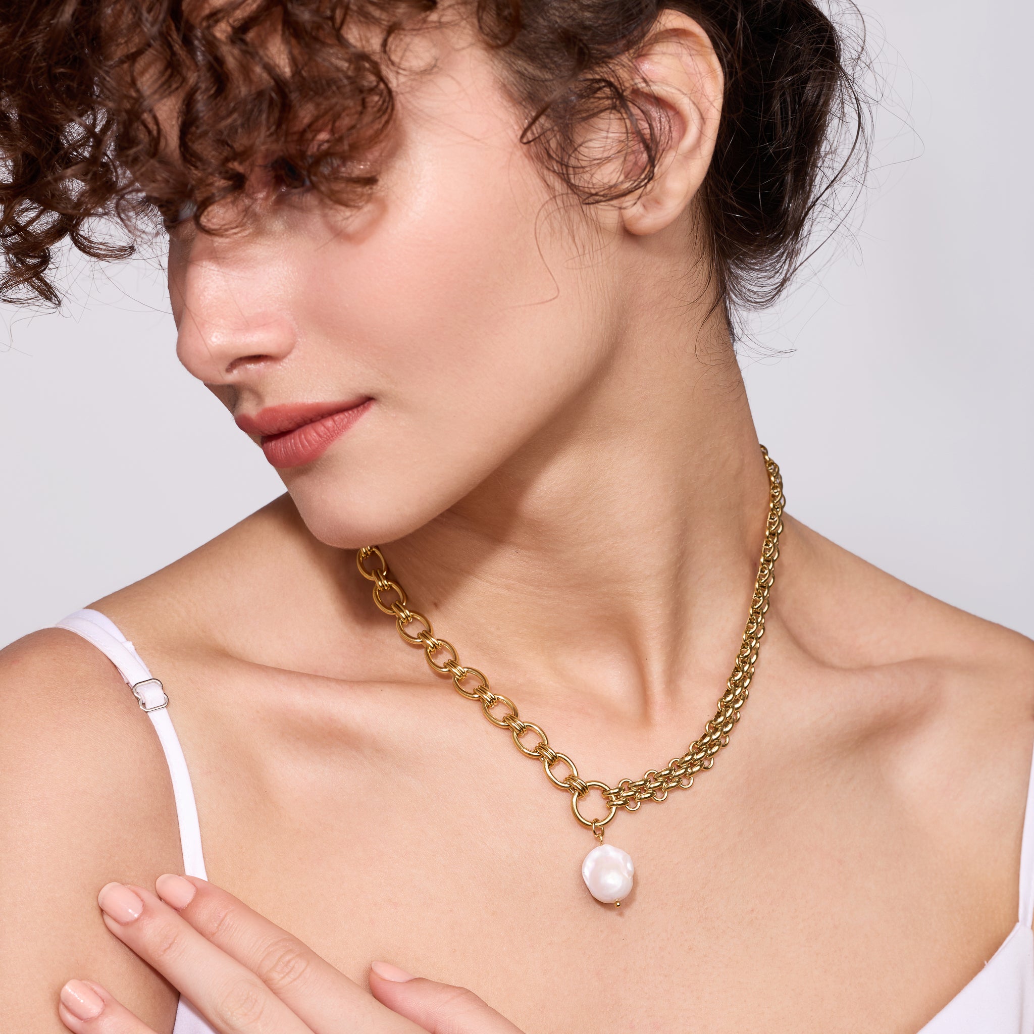 Woman wearing a gold chain necklace with a pearl pendant on a plain background