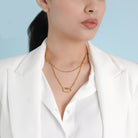 A model wearing the 18K gold-plated layered necklace with interlocking chains and a lock charm, styled elegantly with a white blazer against a soft blue background.