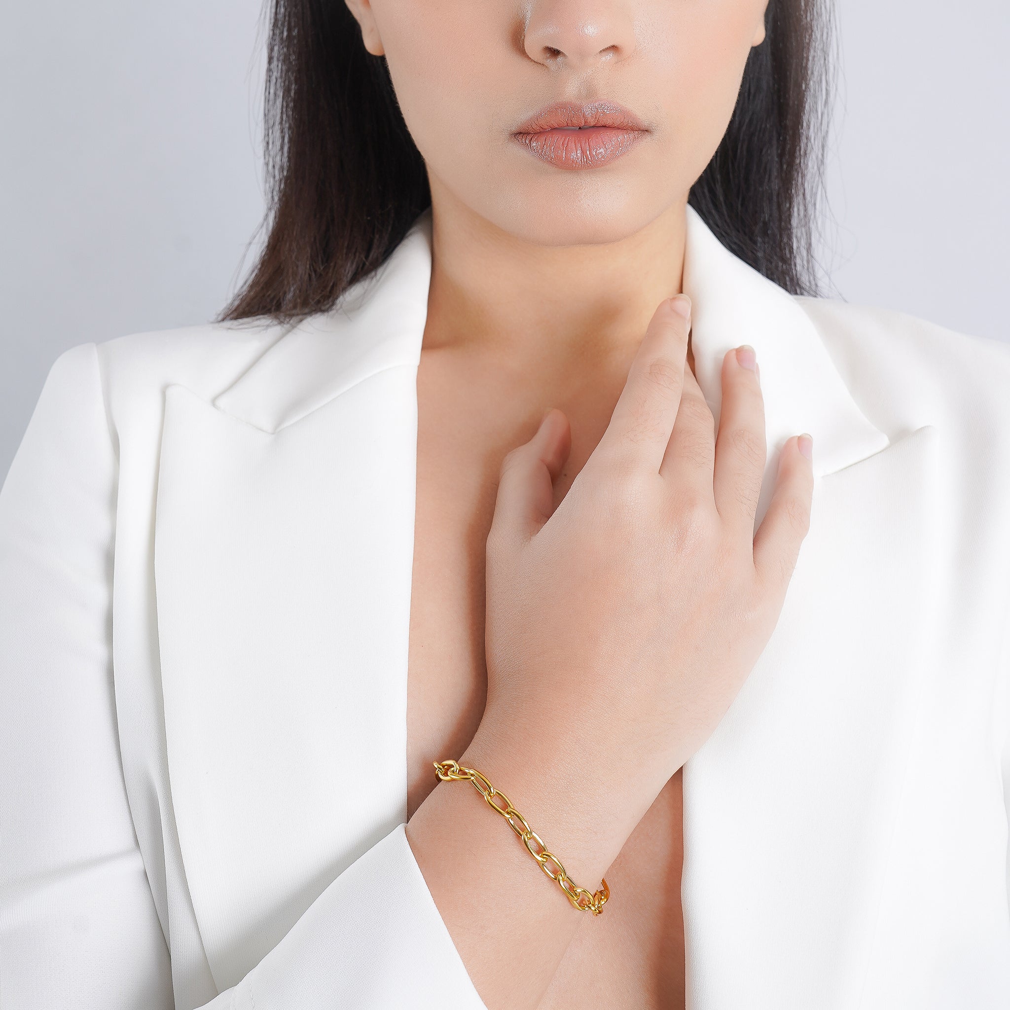 A woman wearing an 18K gold-plated chain-link bracelet on her wrist, styled with a white blazer, showcasing elegance and simplicity.
