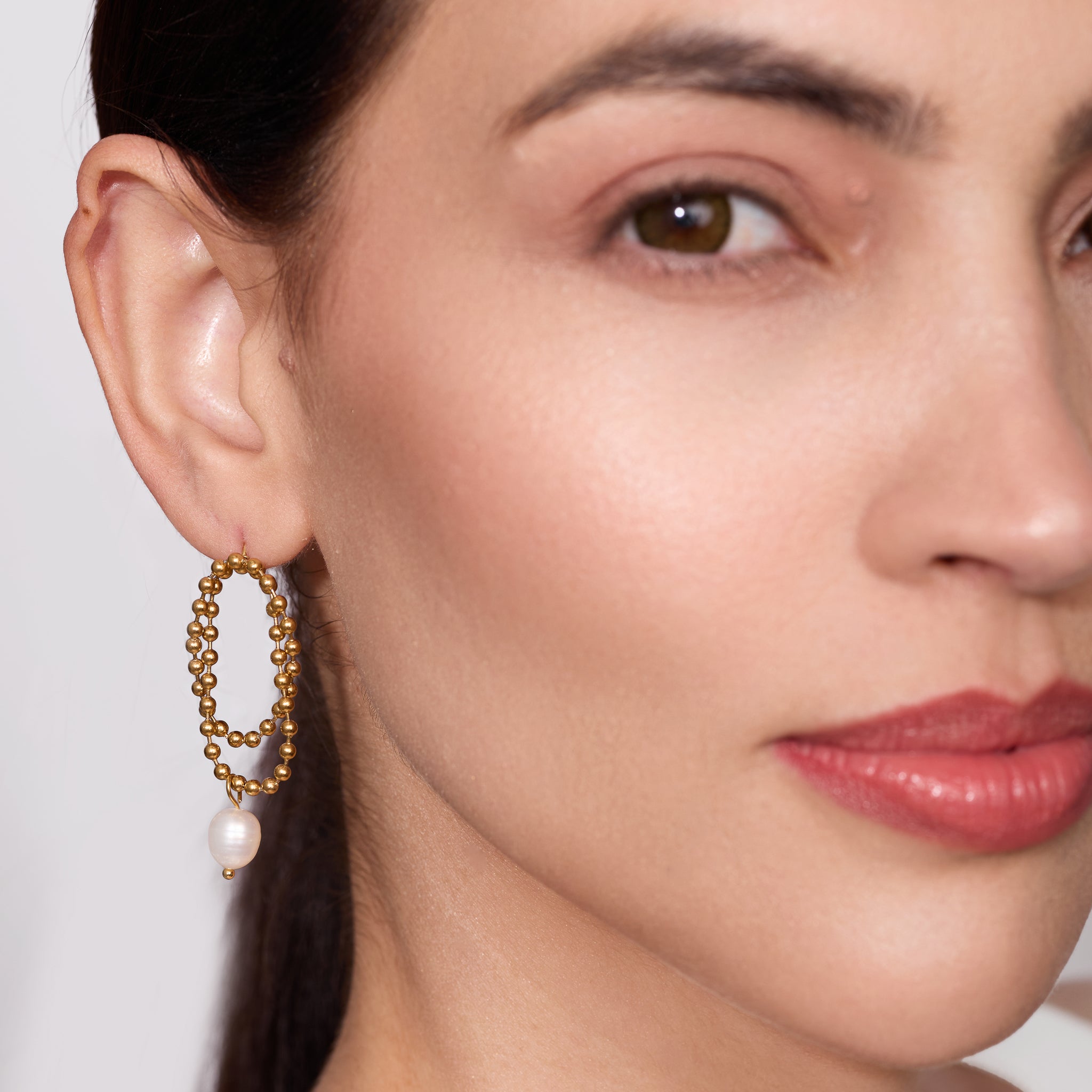 Close-up of a woman wearing gold hoop earrings with pearls.