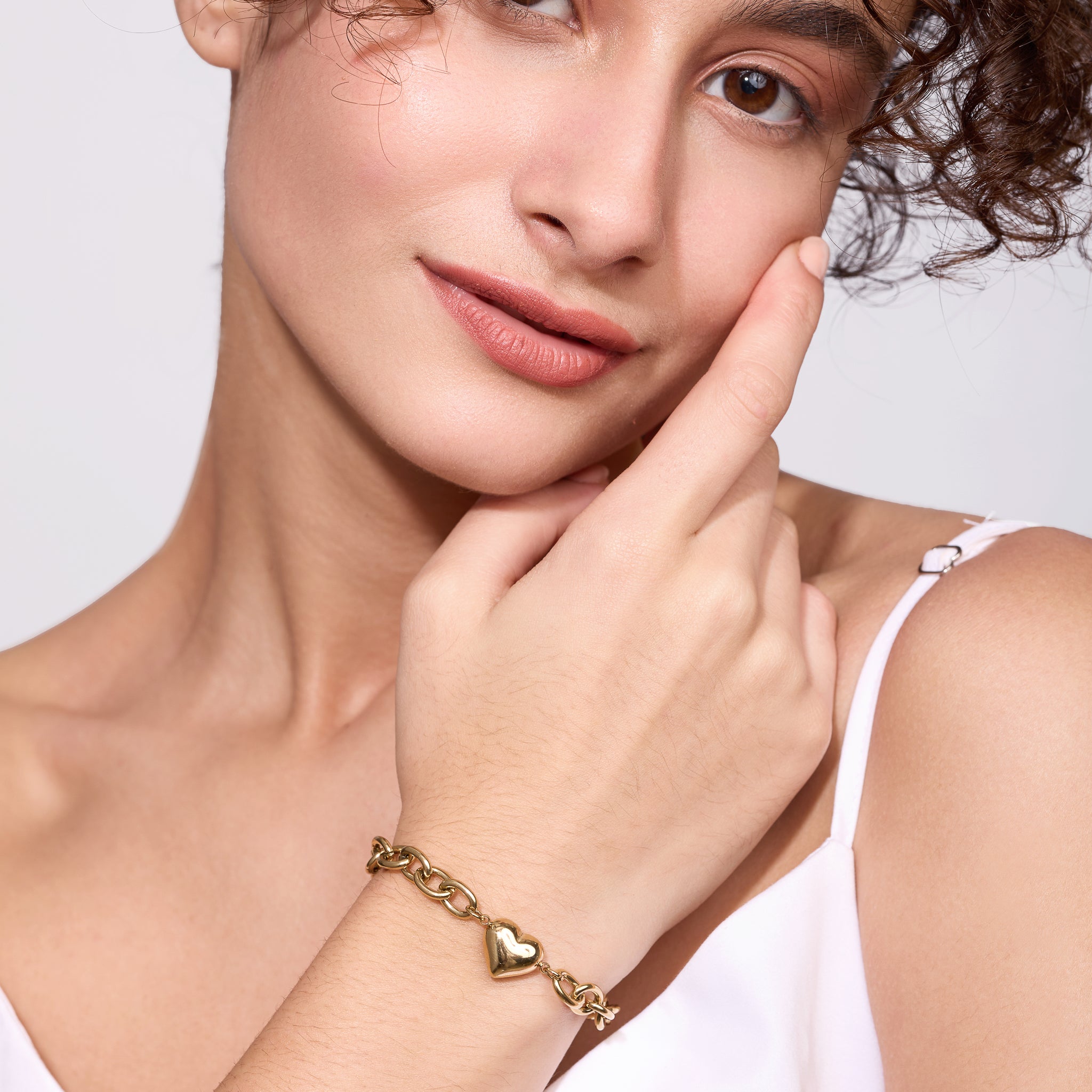 Woman wearing a gold bracelet with heart charms on a light background