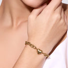 Gold bracelet with heart charm on a wrist against a neutral background