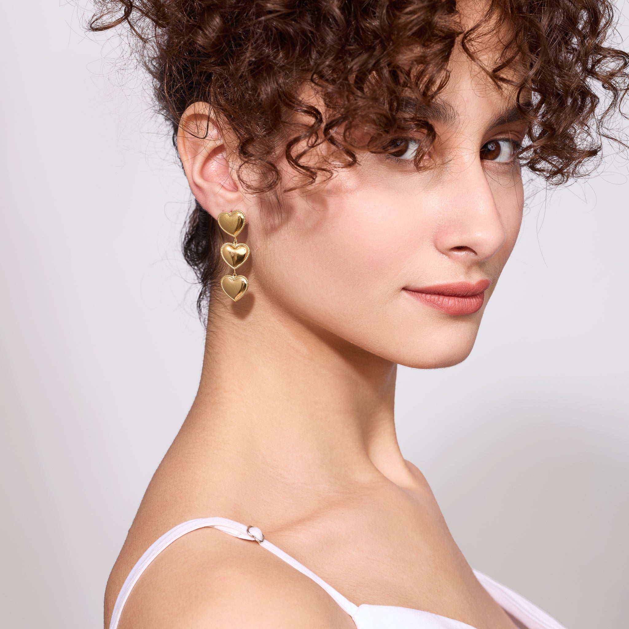 Close-up of a woman wearing gold heart-shaped earrings against a light background