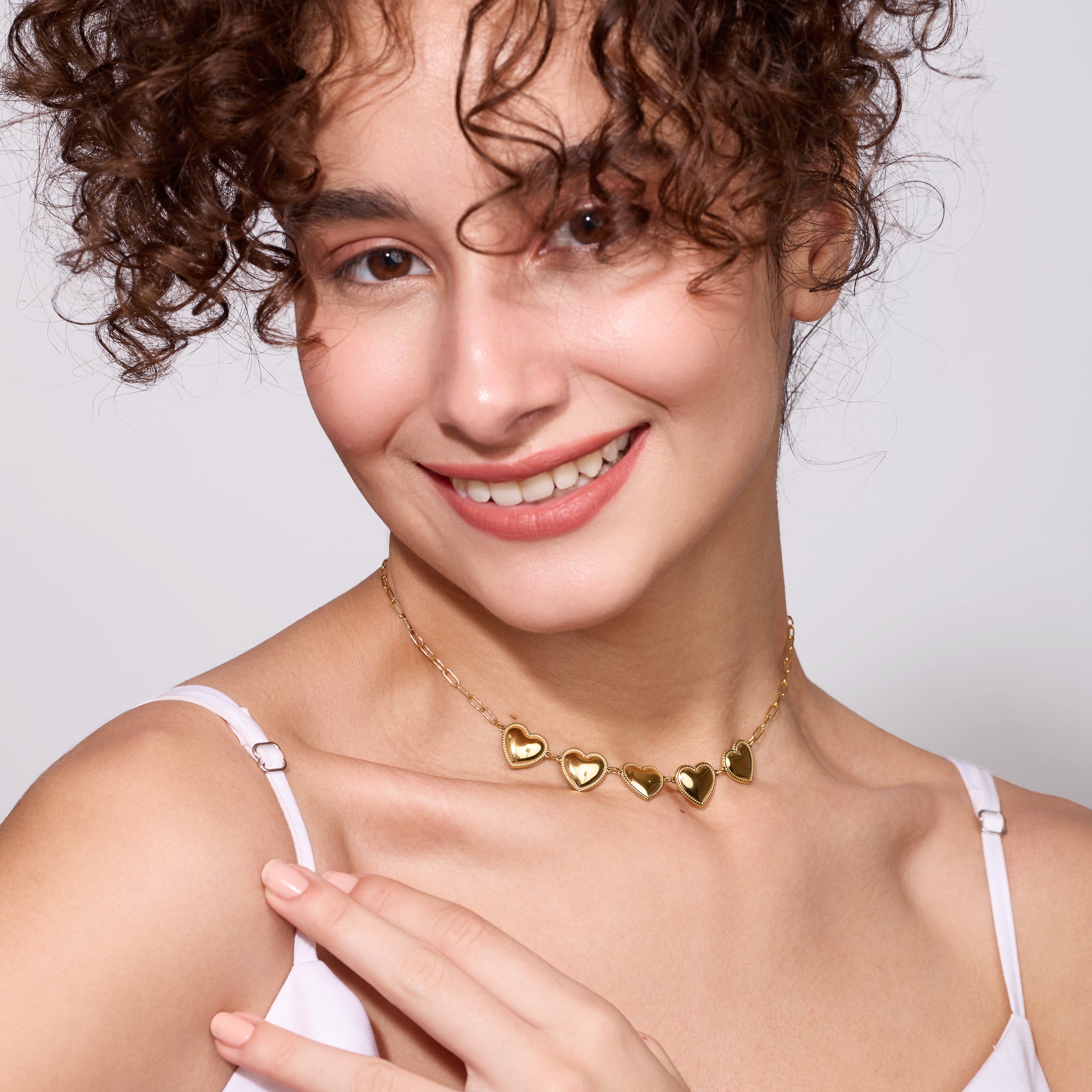 Woman wearing a gold heart-shaped necklace on a plain background