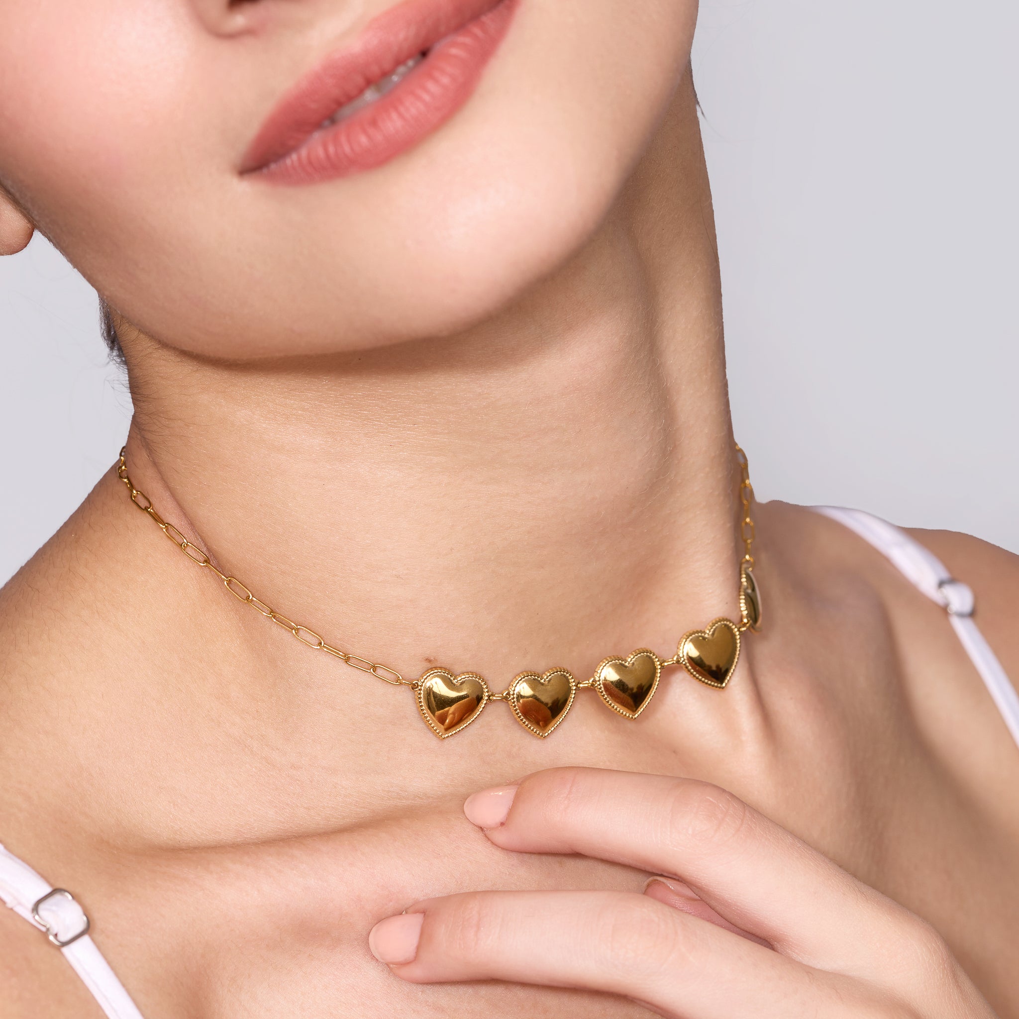 Gold heart-shaped necklace worn by a women with a neutral background