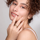 Woman with curly hair wearing gold ring with stones against a plain background