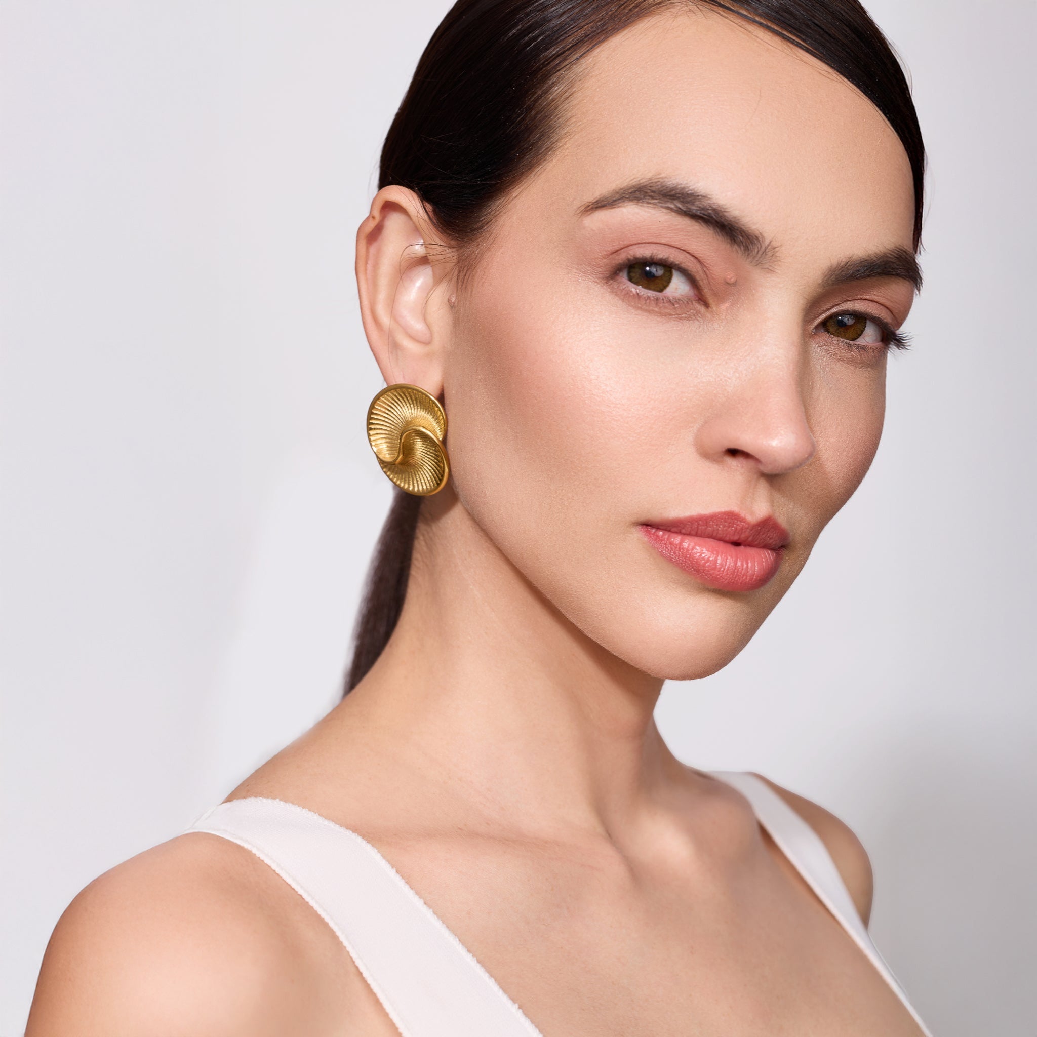 Woman wearing gold earrings against a plain background