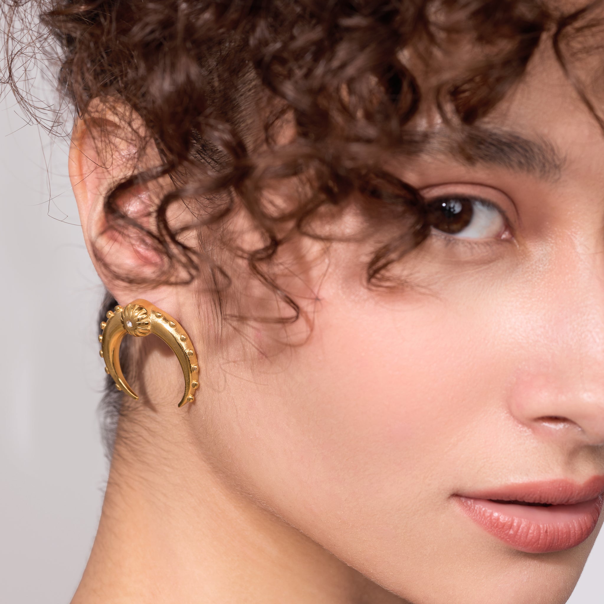 Close-up of a woman wearing a gold earring with a gray background