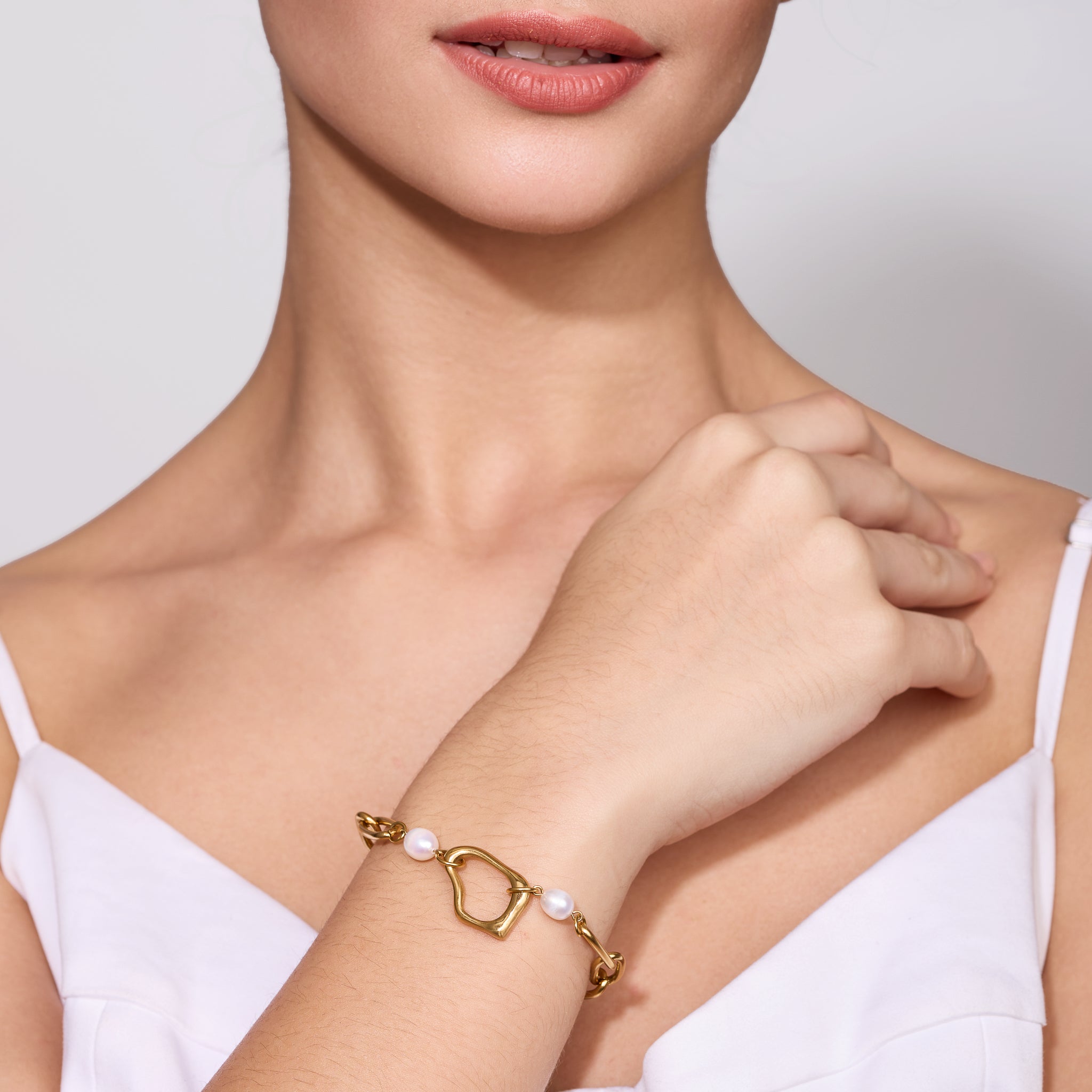 Woman wearing a gold bracelet with pearls on a plain background