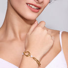 Woman wearing a gold bracelet with a pearl charm on a plain background