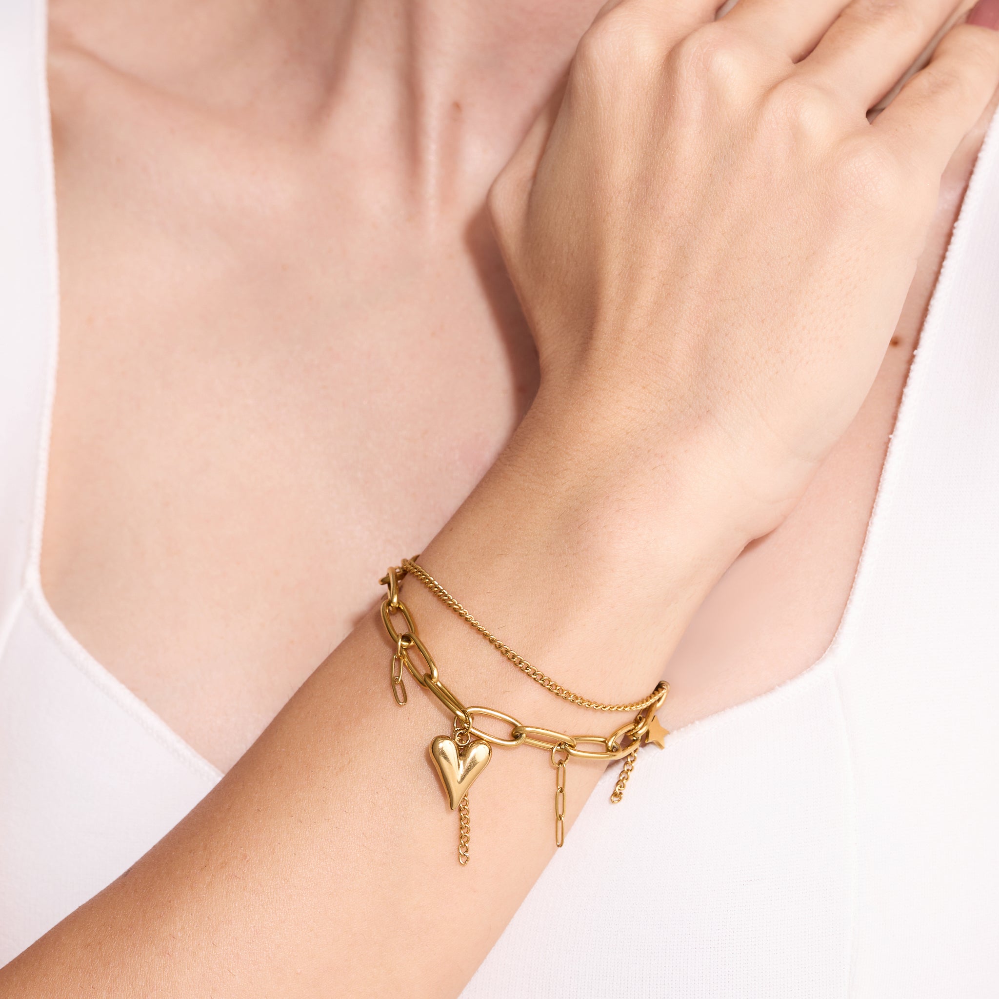 Gold bracelet with heart charm on a wrist against a light background