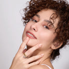 Woman with curly hair wearing two toned ring against a plain background