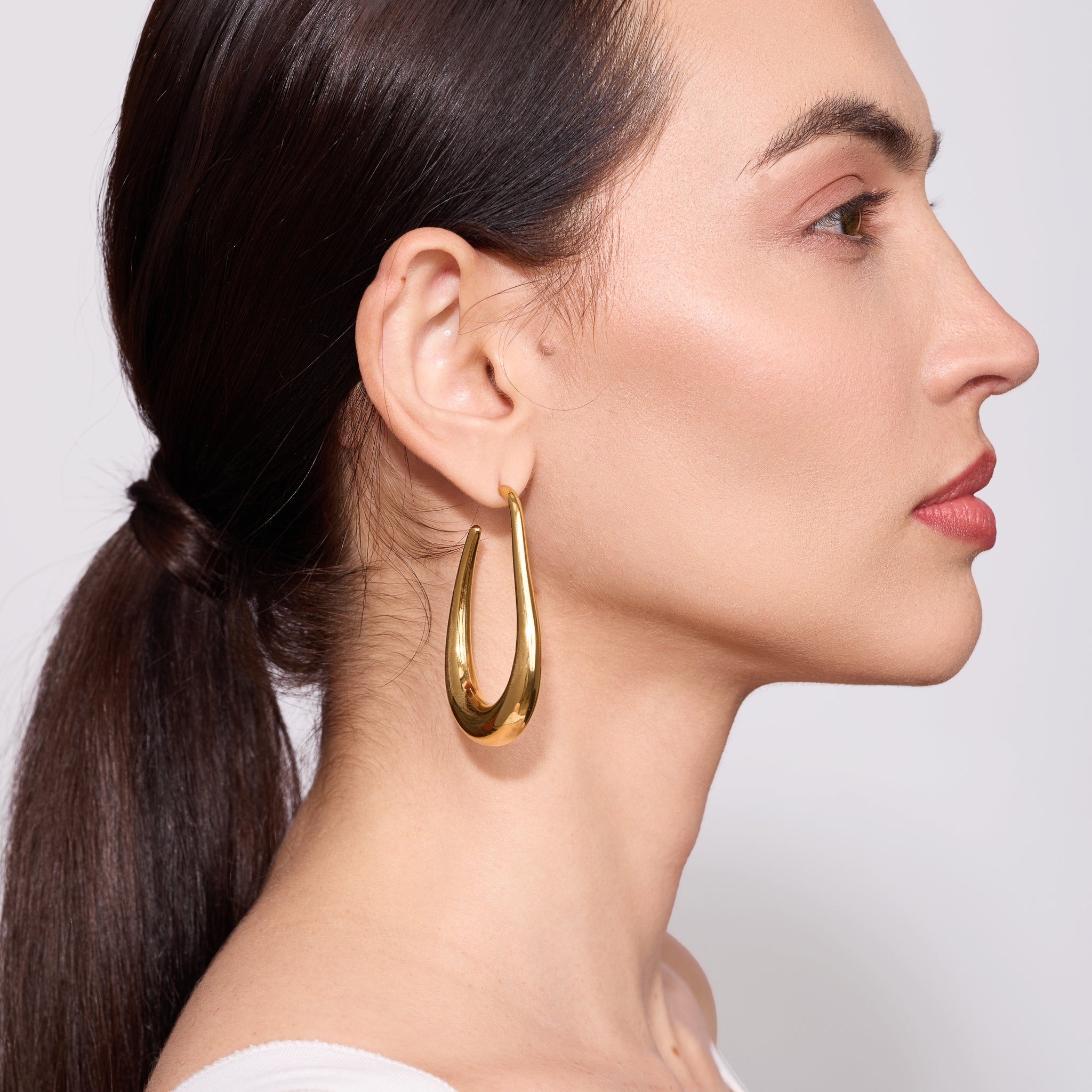 Woman wearing gold hoop earrings with a plain background
