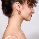 Woman wearing a gold earring on a plain background