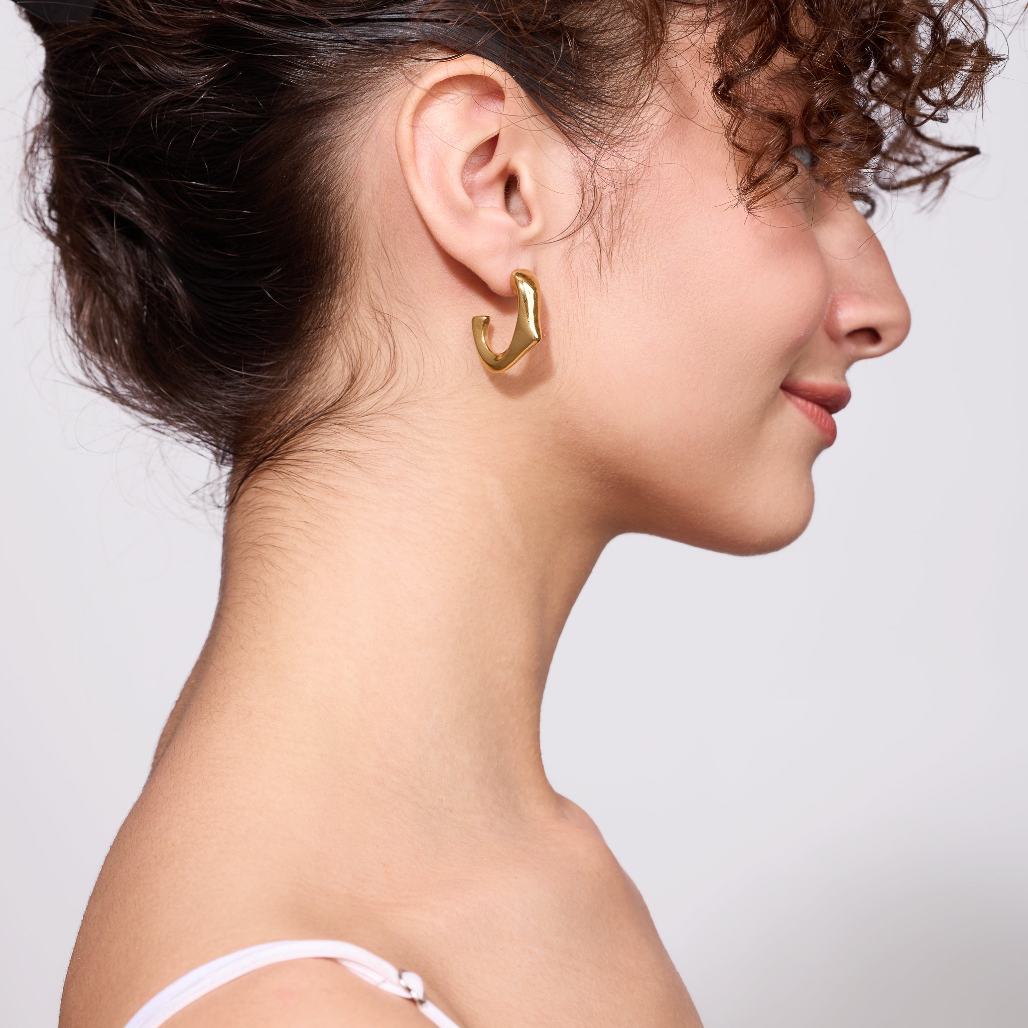 Woman wearing a gold earring on a plain background