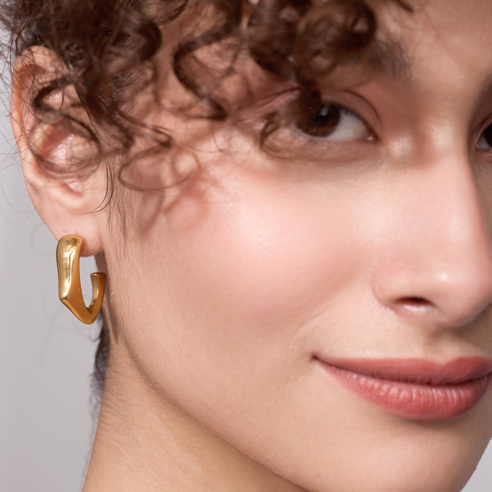 Close-up of a person wearing gold hoop earrings with a neutral background