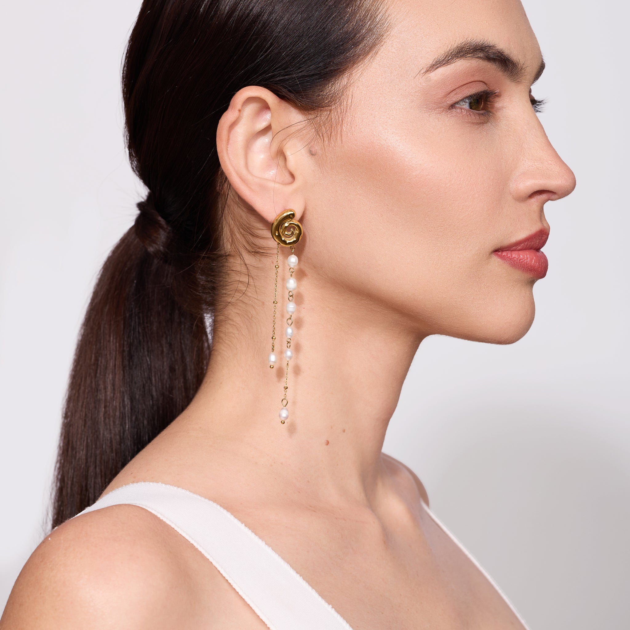 Woman wearing a gold earring with pearl-like beads on a plain background