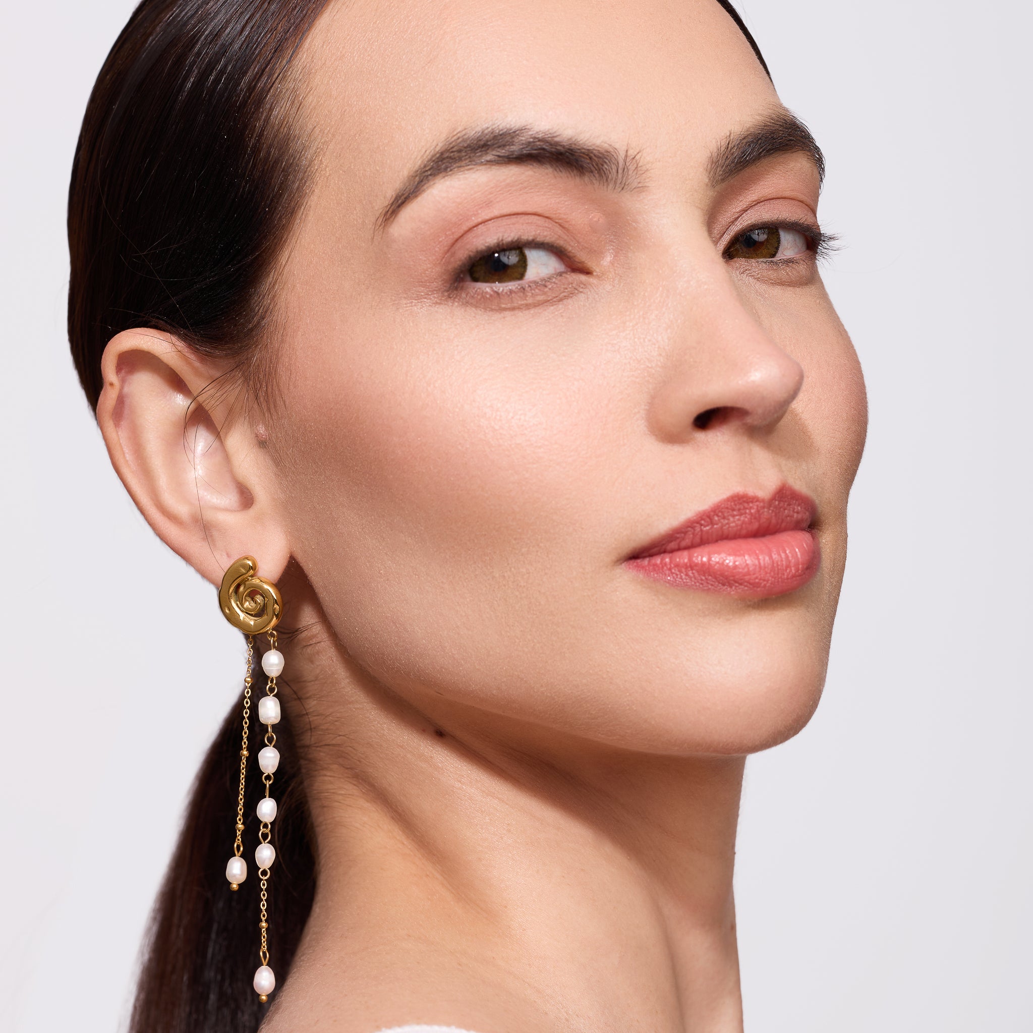 Close-up of a woman wearing a gold earring with pearl drops on a plain background