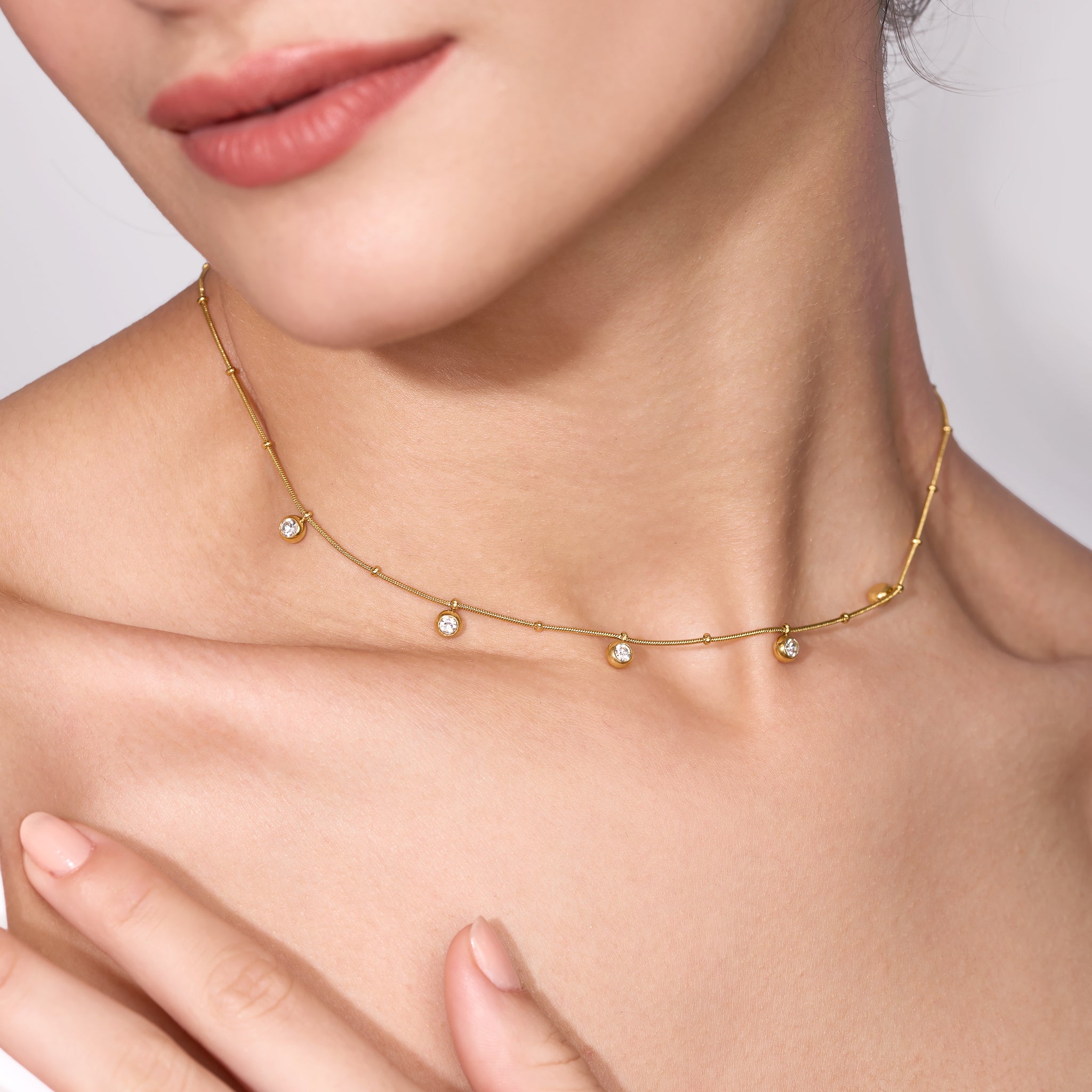 Gold necklace with small diamonds on a person's neck against a neutral background