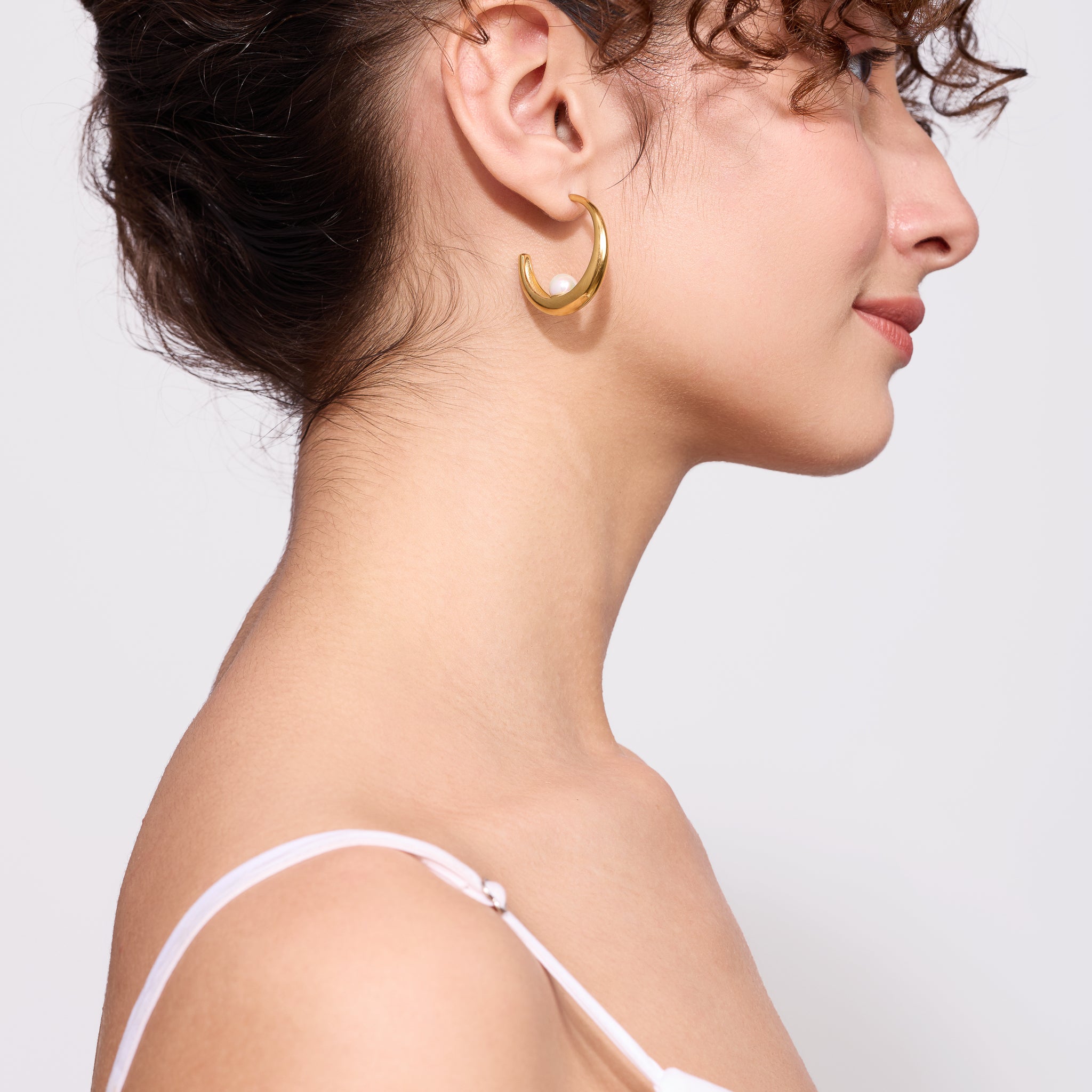 Close-up of a woman wearing a gold hoop earring against a light background