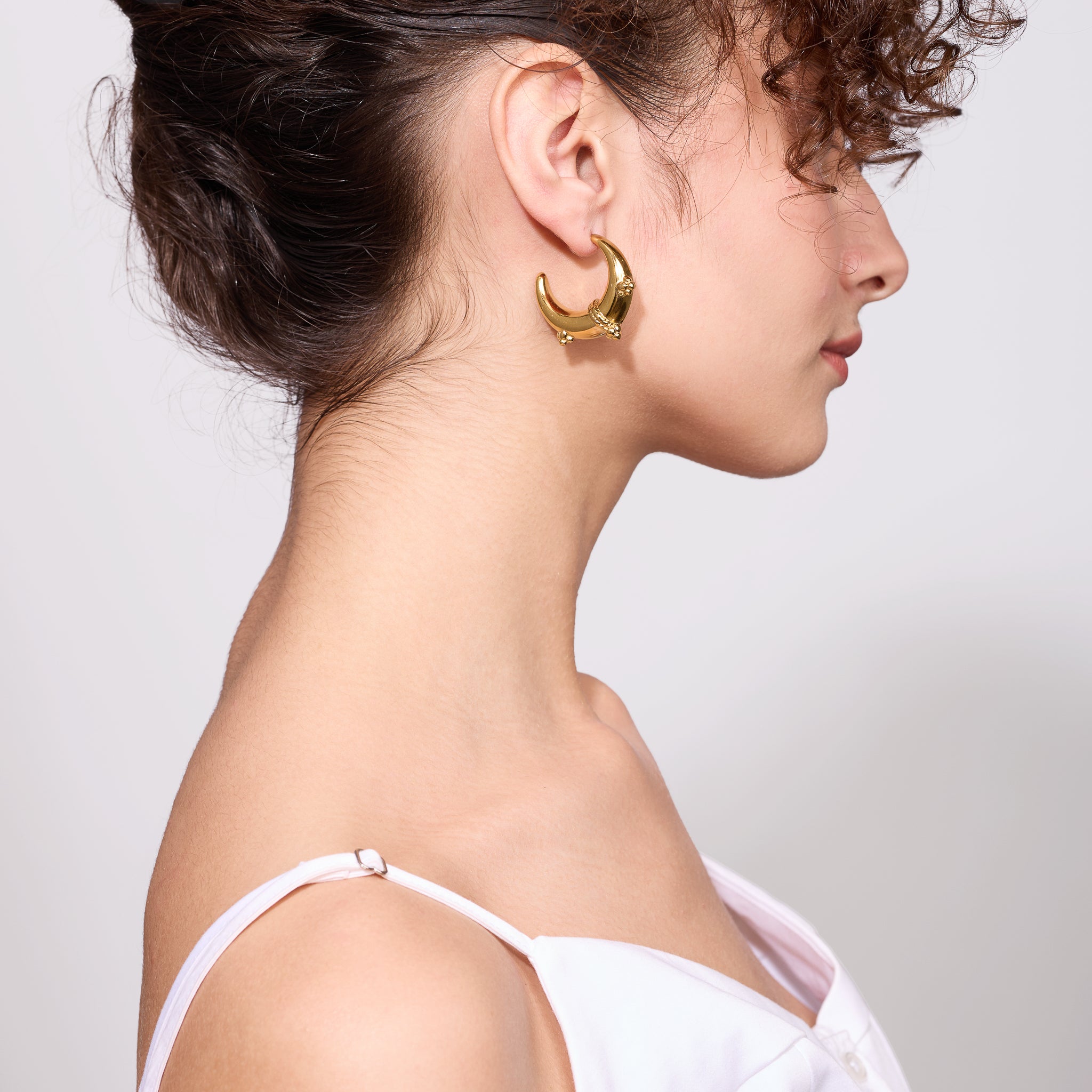 Woman wearing gold hoop earrings with a plain background