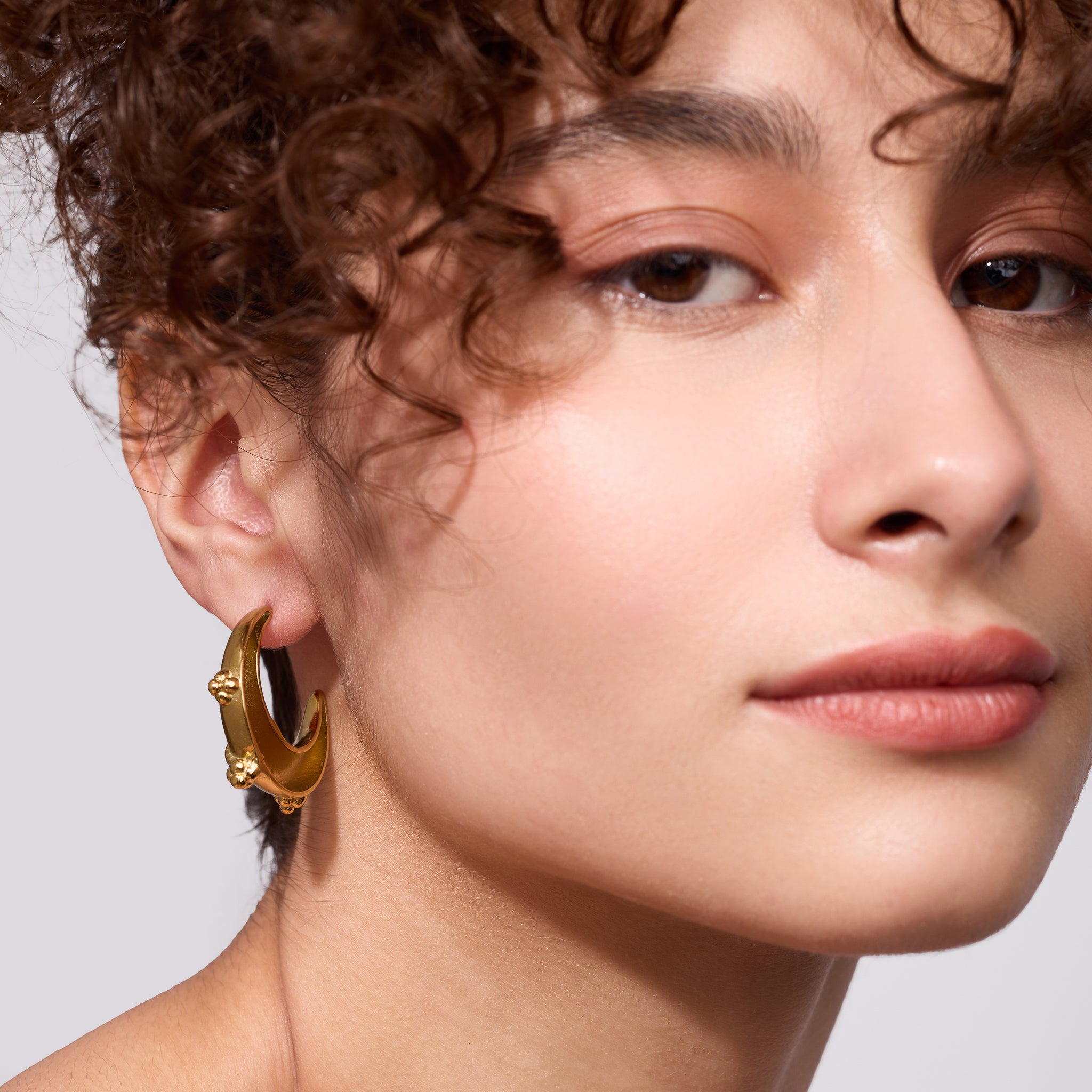 Close-up of a person wearing gold hoop earrings with a neutral background