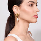 Woman wearing a Gold seahorse-shaped earrings with pearl drops on a plain background