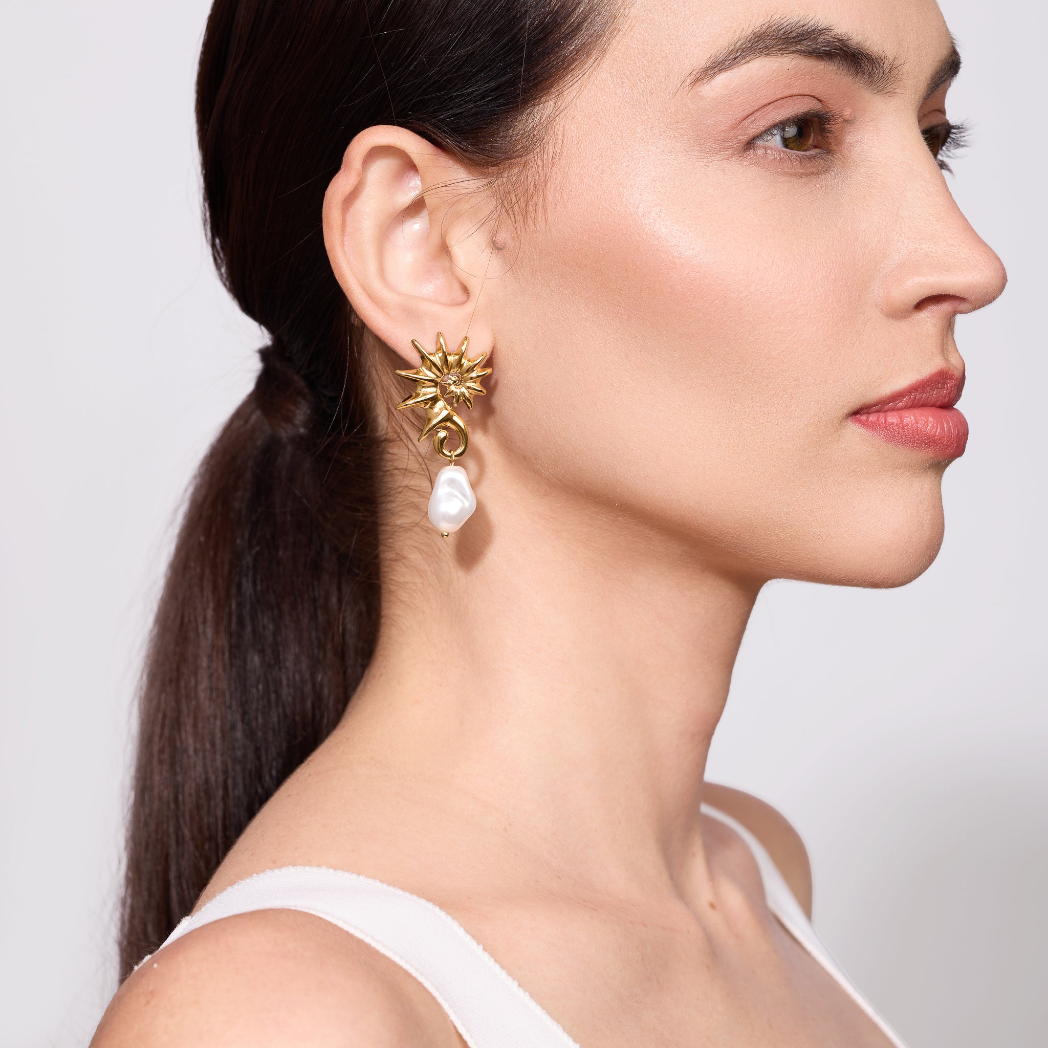 Woman wearing a Gold seahorse-shaped earrings with pearl drops on a plain background