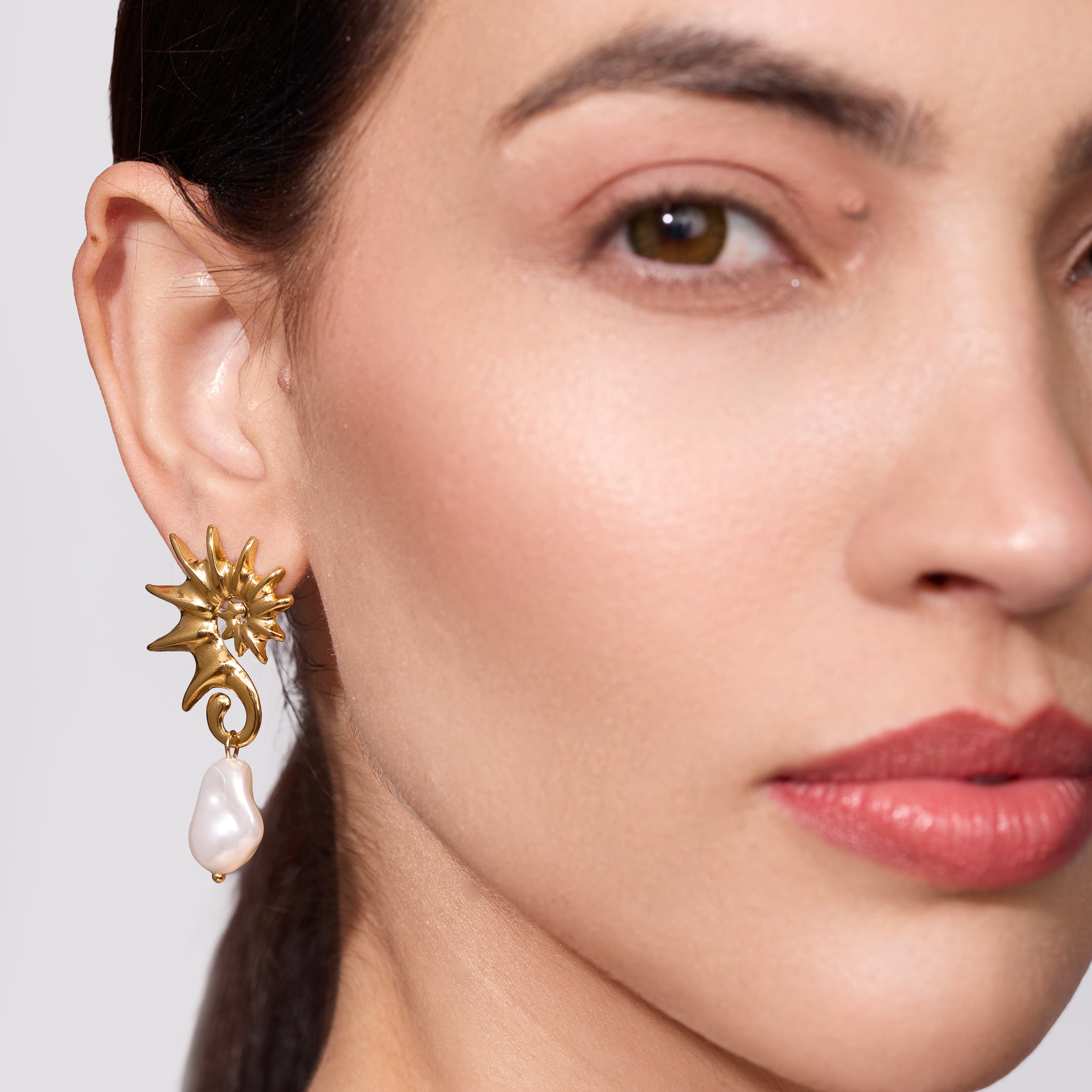 Close-up of a woman wearing a Gold seahorse-shaped earrings with pearl drops on a plain background