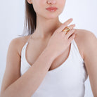 Woman wearing a gold ripple-designed statement ring, styled elegantly with a minimalist white outfit, showcasing its unique texture and layered bands.