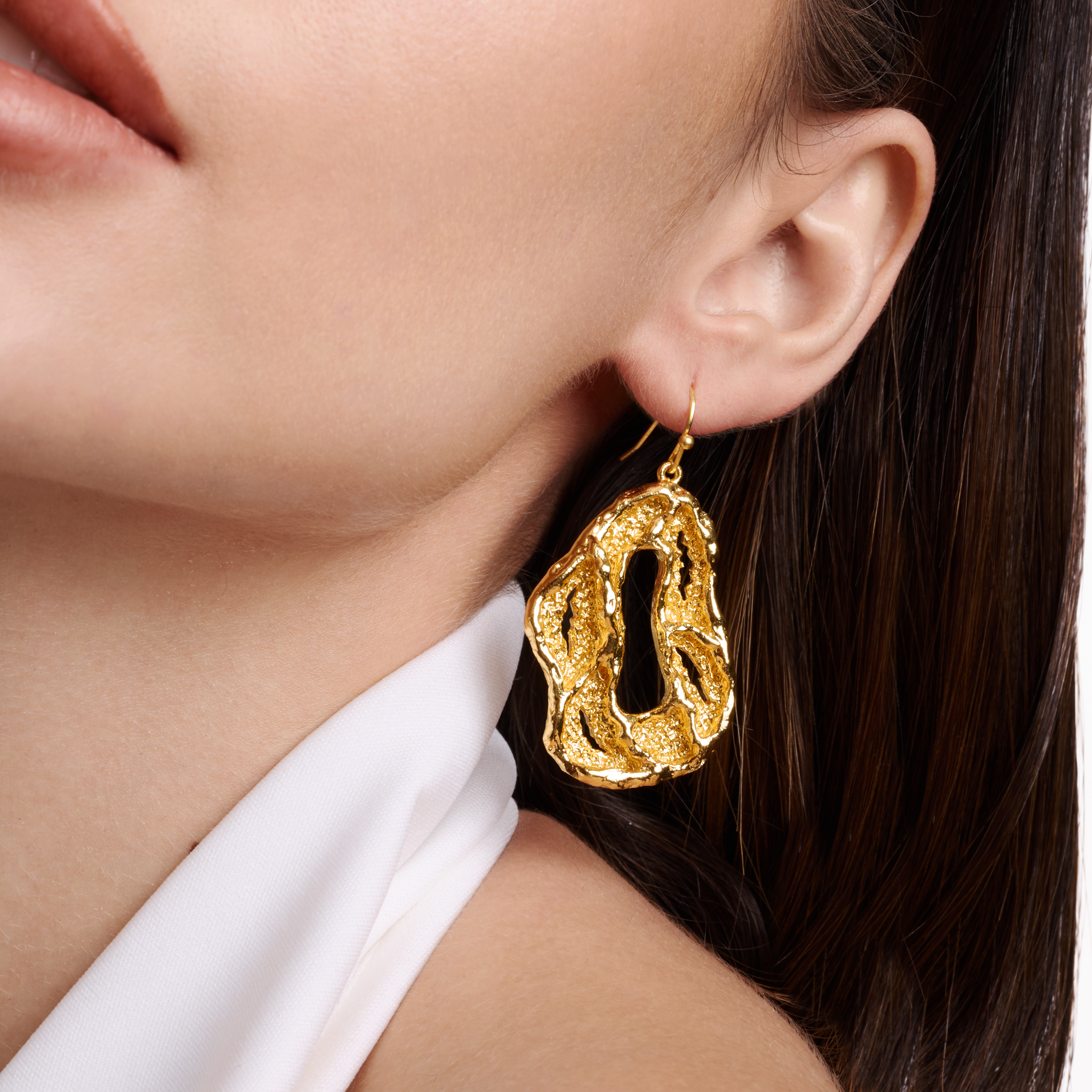 Embrell Becoming Lumen Earrings in 22K gold-plated finish, molten textured open hoop drop earrings, handcrafted demi-fine jewellery, worn by a woman styled in white for an elegant bold look.