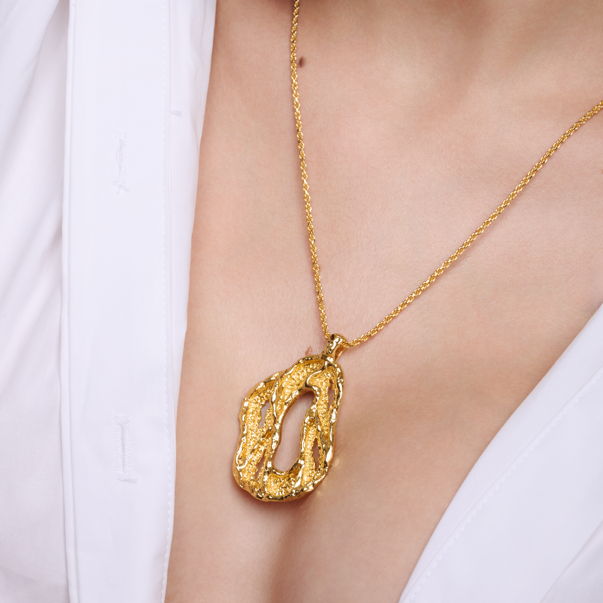 Embrell Becoming Lumen Pendant Necklace in 22K gold-plated finish, handcrafted molten textured open pendant on a fine chain, demi-fine jewellery styled with a white shirt for an elegant bold look.
