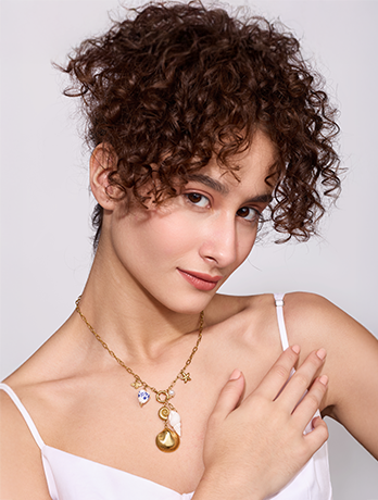 Woman wearing a gold necklace with a pendant against a plain background