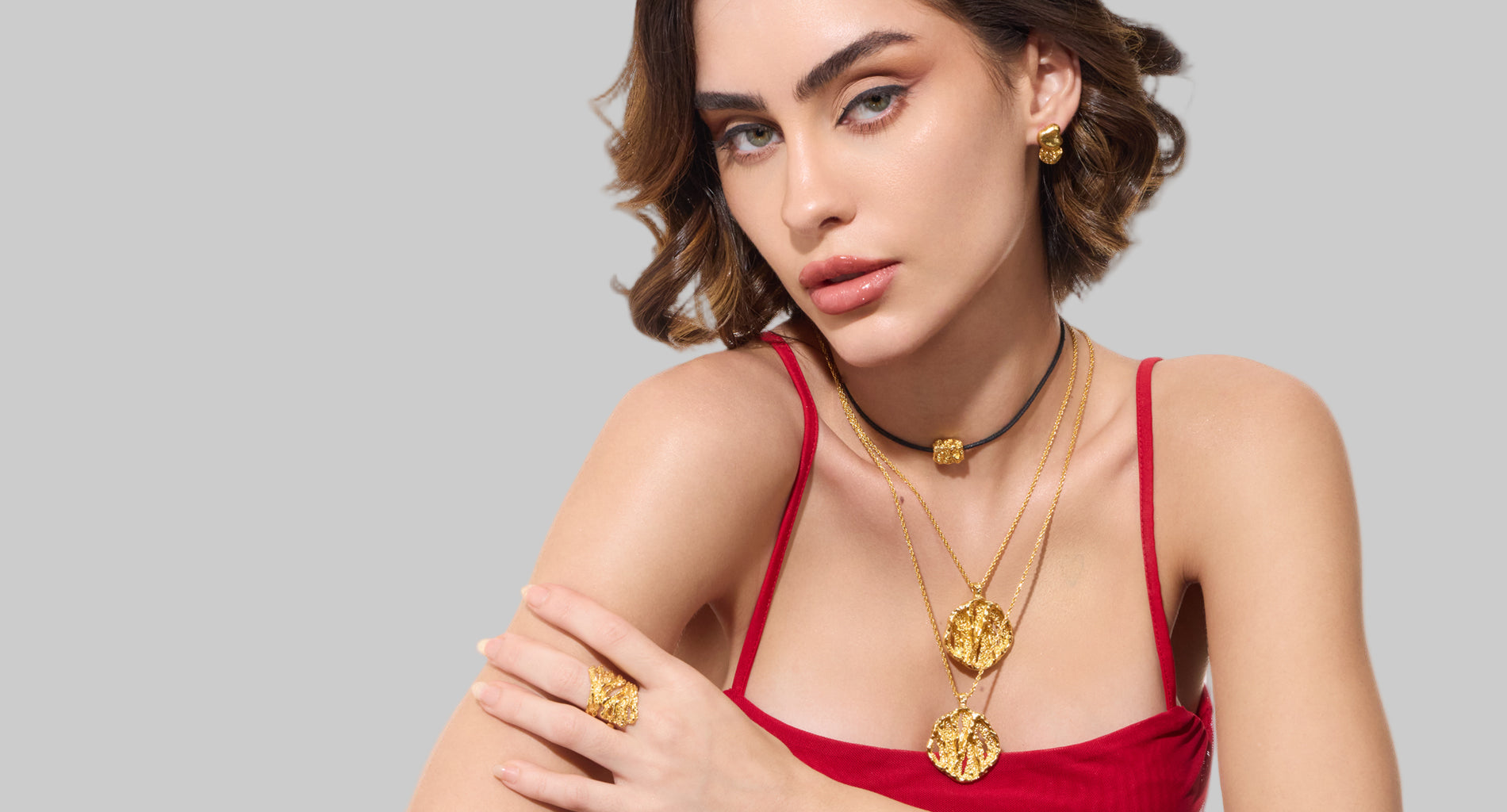 Woman wearing embrell 22K gold jewellery including necklaces and rings on a white background